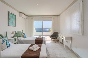 Een hotelkamer met twee bedden, een bureau en uitzicht op zee.