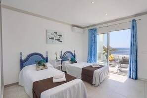 Une chambre d’hôtel avec deux lits, un balcon donnant sur la mer et un tableau accroché au mur.