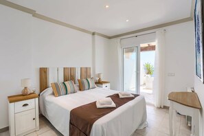A bedroom with a bed, bedside tables, a desk, and a view of the outdoors.