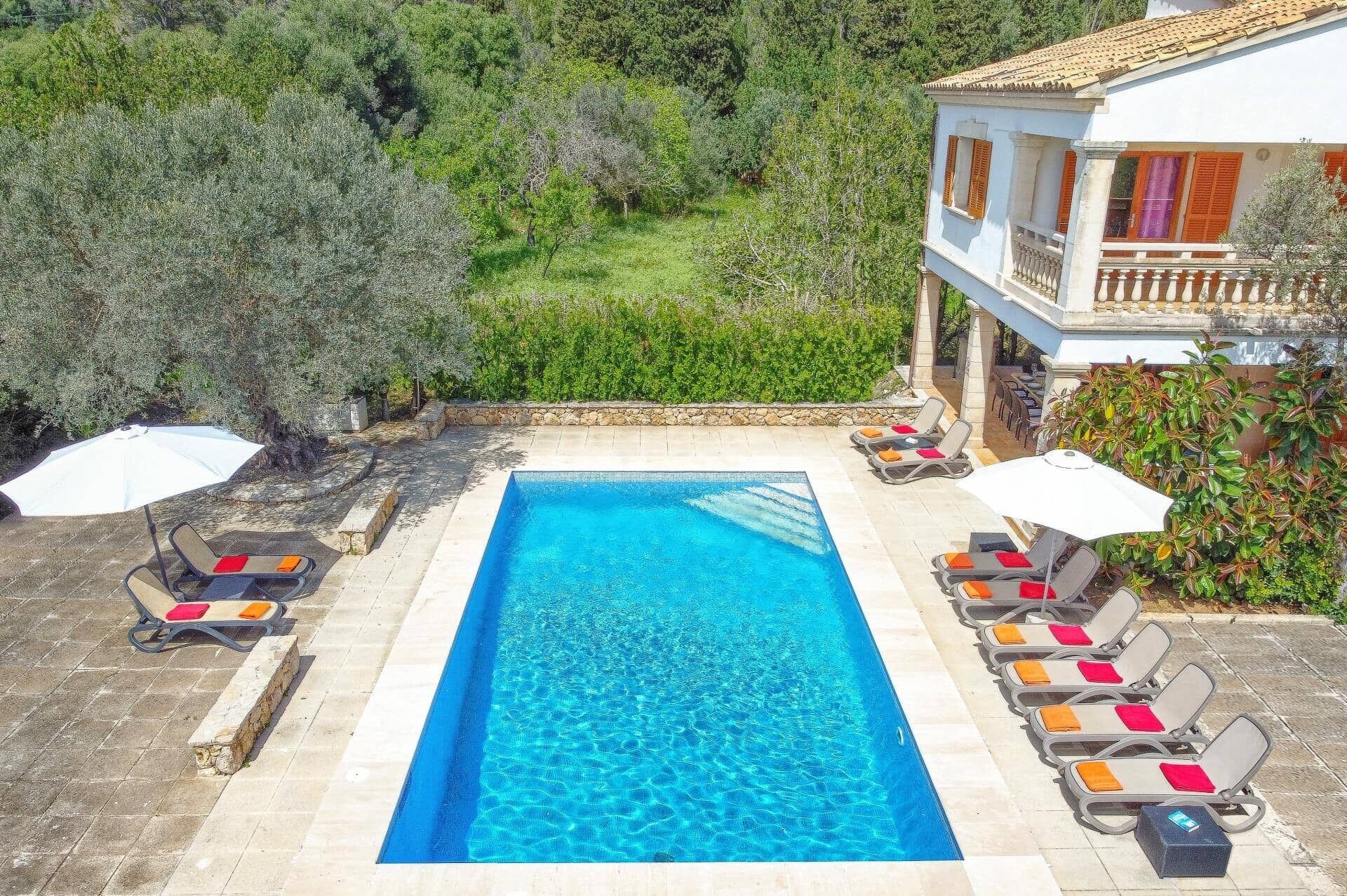 Une piscine rectangulaire à l’eau d’un bleu cristallin, entourée de chaises longues dotées de coussins et bordée d’un mur en pierre.