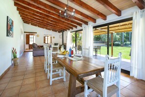 A dining area with a wooden table and white chairs, a chandelier, and a view of a garden through large windows. - Villa Suau Petit by Villa Plus (Mallorca)