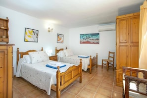 A bedroom with two wooden beds, a chair, a wardrobe, and artwork on the walls.