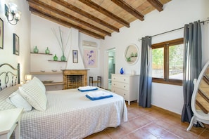 A bedroom with a bed, a fireplace, a dresser, a mirror, and a window with curtains. - Villa Suau Petit by Villa Plus (Mallorca)