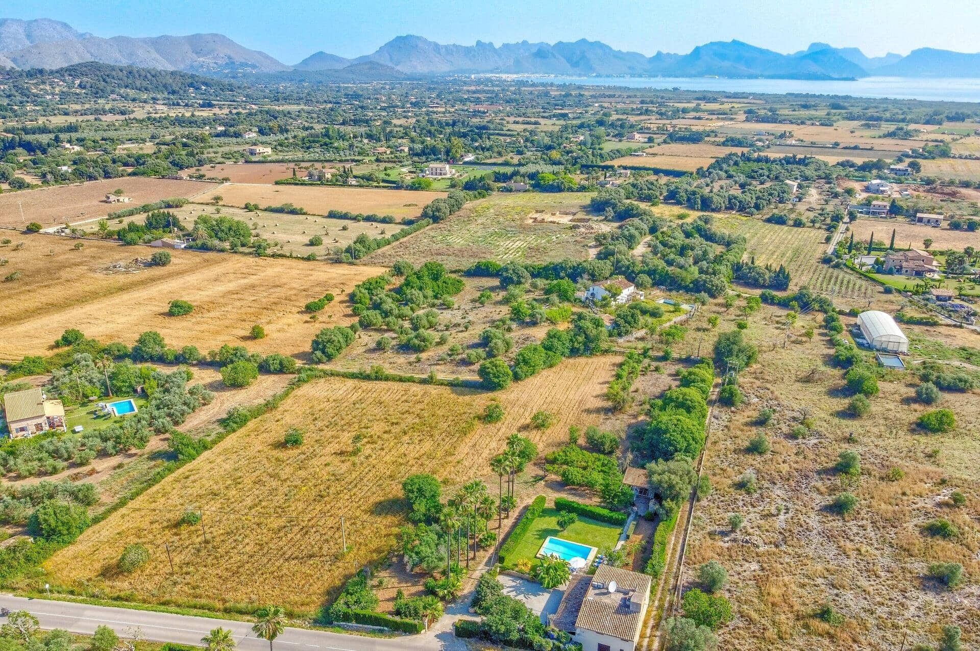 Vista aerea di una zona rurale con campi, case sparse e un ampio specchio d'acqua in lontananza.