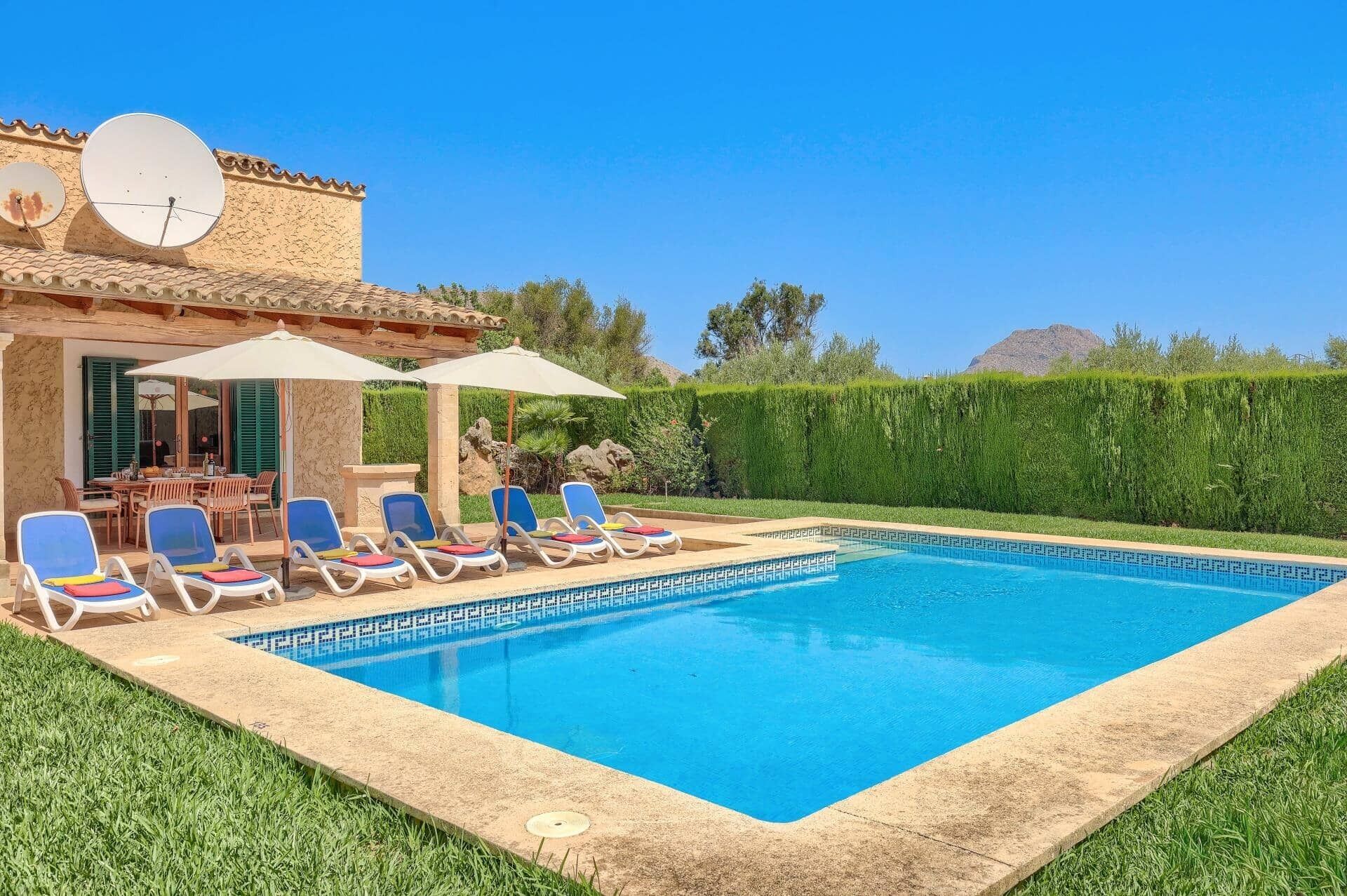 A swimming pool with lounge chairs and umbrellas, surrounded by a well-maintained lawn and a hedge.