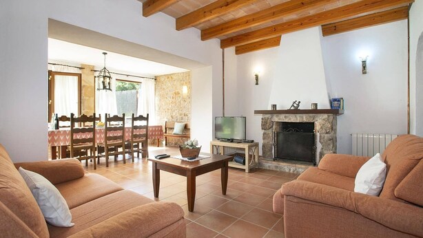 A living room with two sofas, a TV, a fireplace, and a dining area with a table and chairs. - Villa Vidrier II by Villa Plus (El Vilà)