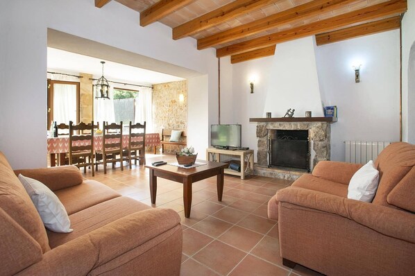 A living room with two sofas, a TV, a fireplace, and a dining area with a table and chairs. - Villa Vidrier II by Villa Plus (El Vilà)