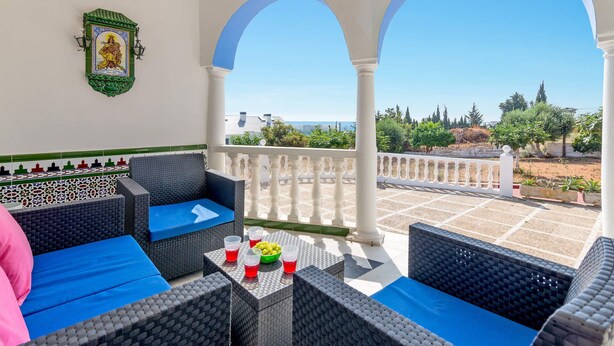 A balcony with wicker furniture, a table with drinks, and a view of the landscape. - Villa Tia Ana by Villa Plus (Fuengirola)