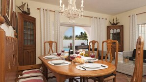A dining area with a wooden table set for four, surrounded by wicker chairs, a chandelier, and nautical-themed decor.