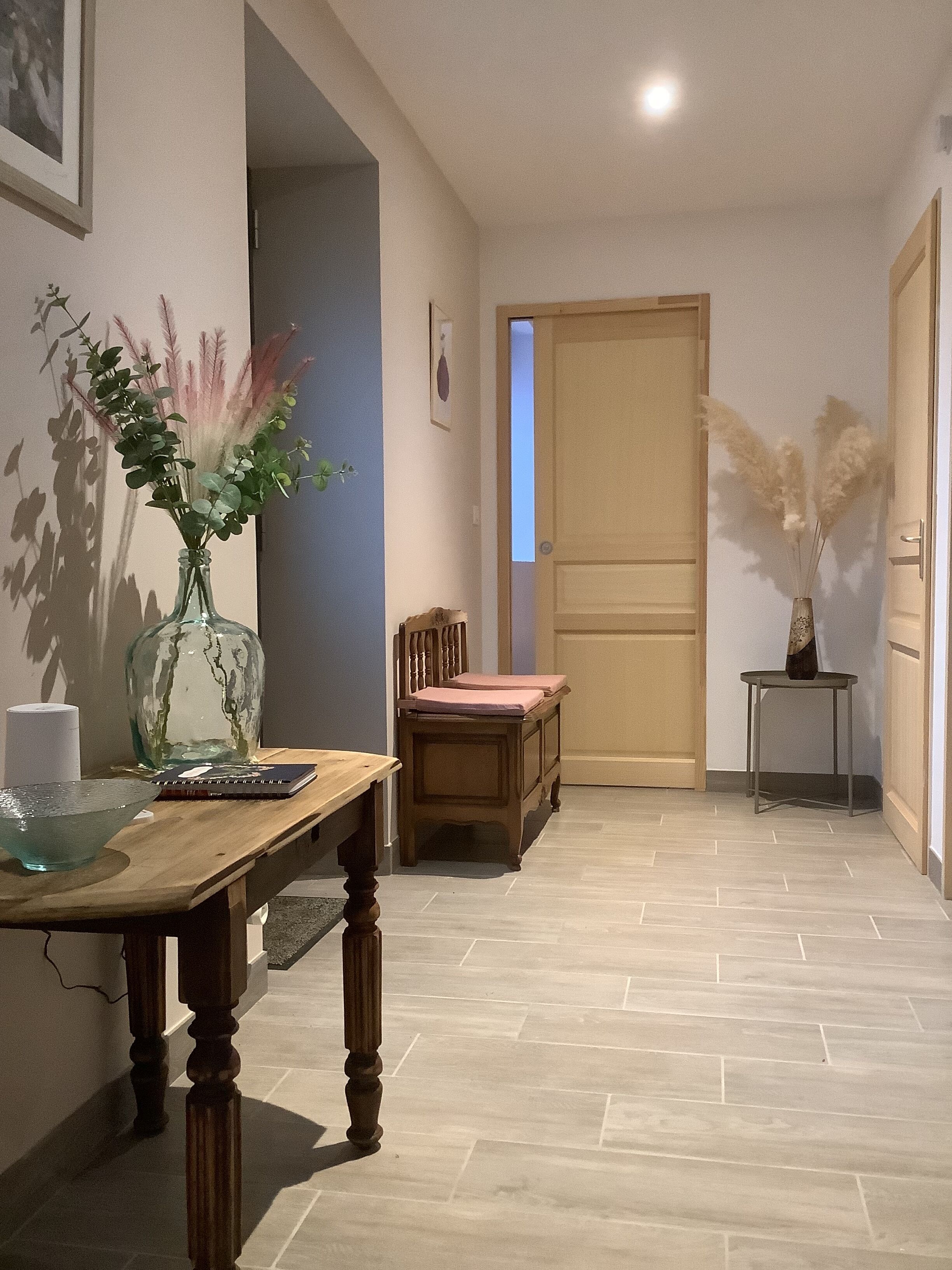 A hallway with a wooden table, chairs, a vase with plants, and a door.