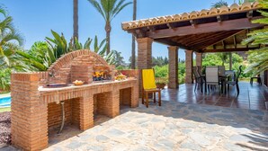 Une terrasse extérieure dotée d’un barbecue en briques, d’un revêtement de sol en pierre et d’un espace salon couvert agrémenté d’une pergola.