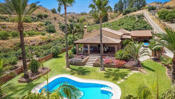 Une maison avec une piscine, entourée d’un jardin bien entretenu et de palmiers.
