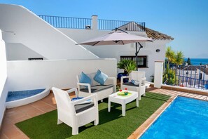 Un espace aménagé au bord de la piscine, avec des meubles en osier blanc, une piscine et une vue sur la mer.