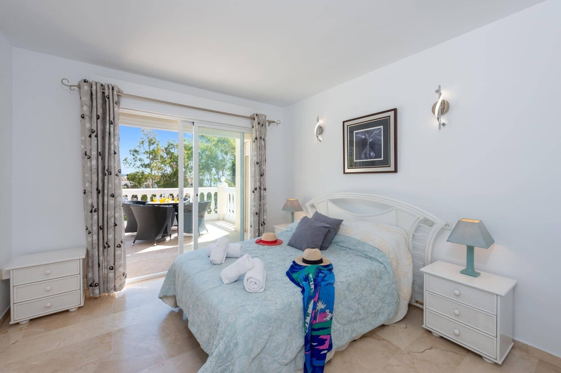 A bedroom with a bed, bedside tables, a window with curtains, and a view of the outside.