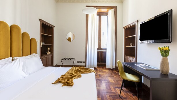 A hotel room with a bed, a desk, a chair, a television, and a mirror.