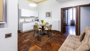 A modern kitchen with white cabinets, a dining table with chairs, and a wooden herringbone floor.