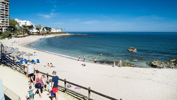 A beach with clear blue water, a wooden walkway, and beach chairs.