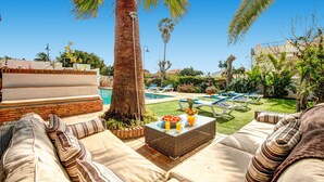 A poolside area with a wicker table, lounge chairs, and a palm tree.