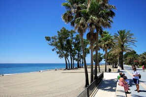 A beach with palm trees, a clear blue sky, and a calm sea. - Villa Cortijo Viejo by Villa Plus (San Pedro de Alcantara)