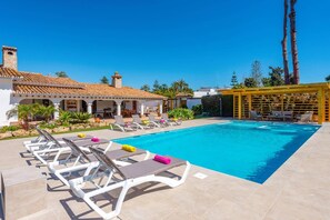 A swimming pool with lounge chairs, a pergola, and a building with a tiled roof. - Villa Ramos by Villa Plus (Atalaya Isdabe)