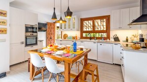 A modern kitchen with white cabinets, a wooden dining table, and a built-in dishwasher.