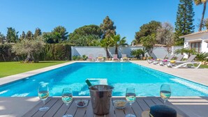 A poolside table with glasses and a hat, overlooking a swimming pool with lounge chairs. - Villa Ramos by Villa Plus (Atalaya Isdabe)