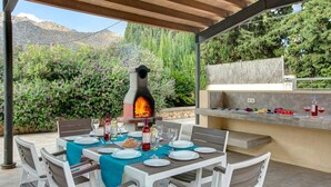 An outdoor dining area with a stone oven, a grill, and a table set for a meal. - Villa Llobiner by Villa Plus (Pollença)
