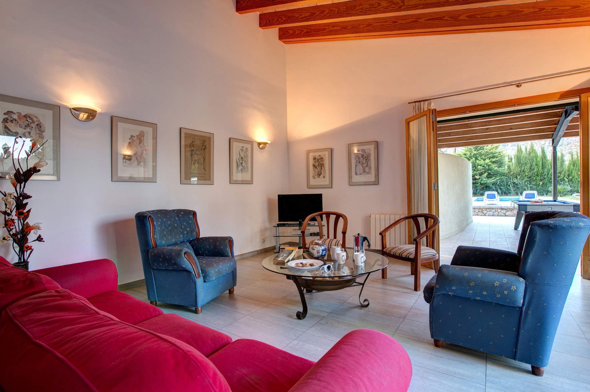 Un salon spacieux avec un canapé rouge, deux fauteuils bleus, une table basse et des œuvres d’art encadrées accrochées aux murs.