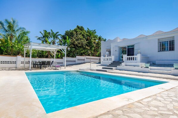A swimming pool with a white building and a covered seating area.