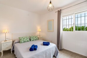 Una camera da letto con un letto, due lampade ai lati, un comodino, uno specchio e una finestra con tende.