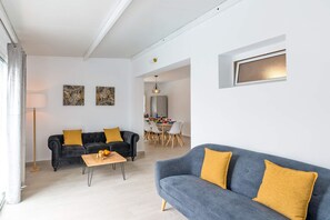 Un soggiorno moderno con un divano grigio, un divano nero con cuscini senape e un tavolino da caffè in legno. Sullo sfondo, una zona pranzo con tavolo apparecchiato per quattro persone.