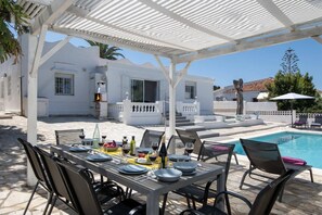 Un espace repas avec vue sur la piscine, des siĂšges dâextĂ©rieur et un barbecue.