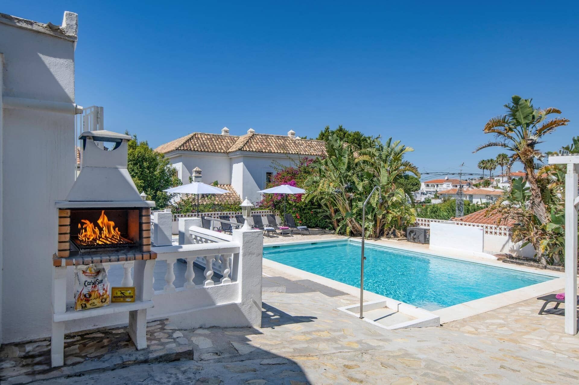 Ein Poolbereich mit Grill, Liegestühlen und Blick auf ein Gebäude mit einem Ziegeldach.