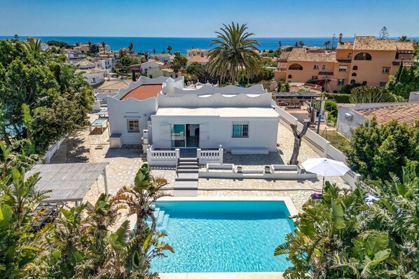 Une villa blanche dotĂ©e dâune piscine, entourĂ©e dâune vĂ©gĂ©tation luxuriante et offrant une vue sur la mer.