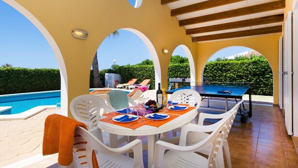 A covered outdoor dining area with a pool, white plastic chairs, and a ping pong table. - Villa Neptune by Villa Plus (Cap d'Artrutx)