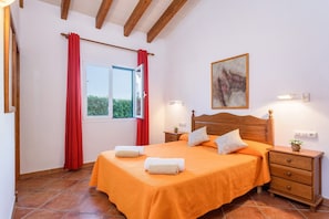 Un dormitorio con cama, mesita de noche, cómoda, ventana con cortinas rojas y un cuadro en la pared.
