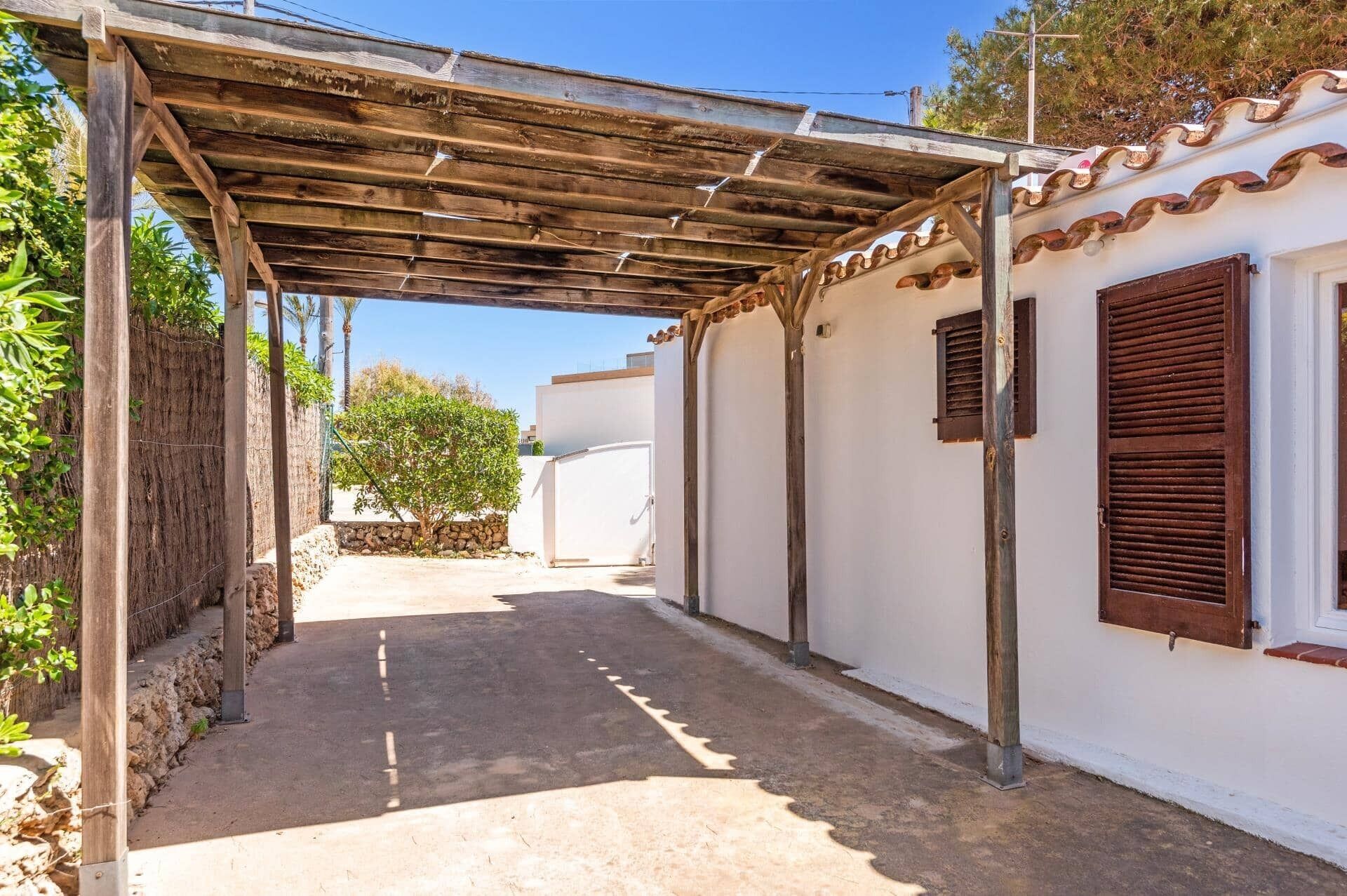 Un espace extérieur abrité, avec un chemin en béton menant à un bâtiment blanc aux volets bruns.