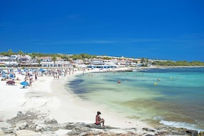 A beach with clear waters, a sandy shore, and buildings in the background. - Villa Iris Prima by Villa Plus (Punta Prima)
