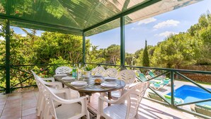 An outdoor dining area with a covered table and chairs, overlooking a swimming pool and lush greenery. - Villa Serafina by Villa Plus (Son Parc)