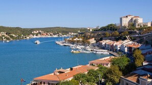 A coastal town with a marina, buildings with red-tiled roofs, and a prominent white building on a hill. - Villa Serafina by Villa Plus (Son Parc)