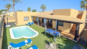 Ein modernes Haus mit Swimmingpool, Sitzgelegenheiten im Freien und Palmen.