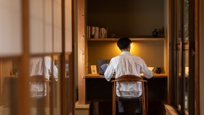 A person seated at a wooden desk with a laptop, surrounded by bookshelves. - TEMPLESTAY ZENSO (Chiyoda Town, Oura District)