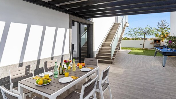 An outdoor patio with a table set for two, a pool table, and a staircase leading to an upper level. - Villa Lola by Villa Plus (Corralejo)