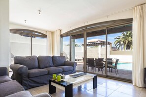 Una sala de estar moderna con un sofá gris, una mesa de centro y vistas a una piscina y zona de estar al aire libre.