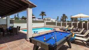 A pool area with a pool table, lounge chairs, and a covered seating area. - Villa Jenny by Villa Plus (Corralejo)