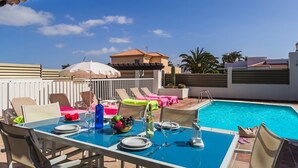 A rooftop pool area with lounge chairs, a dining table set for two, and a clear blue sky. - Villa Sirena by Villa Plus (Corralejo)