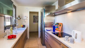 A modern kitchen with stainless steel appliances, a white countertop, and a view into the dining area. - Villa Sirena by Villa Plus (Corralejo)