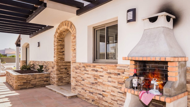 A patio with a stone fireplace, a window, and a pergola. - Villa Sirena by Villa Plus (Corralejo)