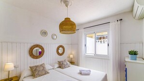 Een hotelkamer met twee bedden, een raam met uitzicht, een hanglamp en een kleine plant op een kastje.