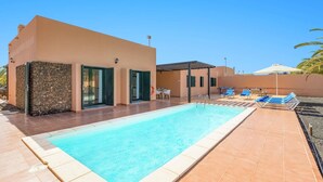 A swimming pool with a sun terrace, a covered seating area, and a stone wall. - Villa Palm View by Villa Plus (Corralejo)